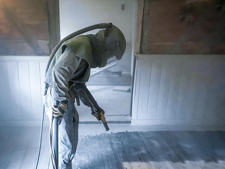 Man wearing protective gear shot blasting a floor in a building.