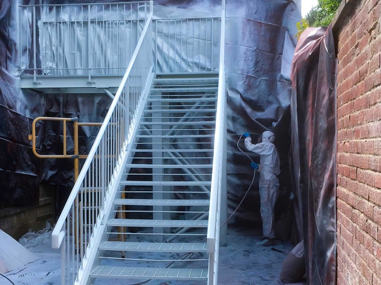 Man wearing protective overalls wet spraying a large staircase.